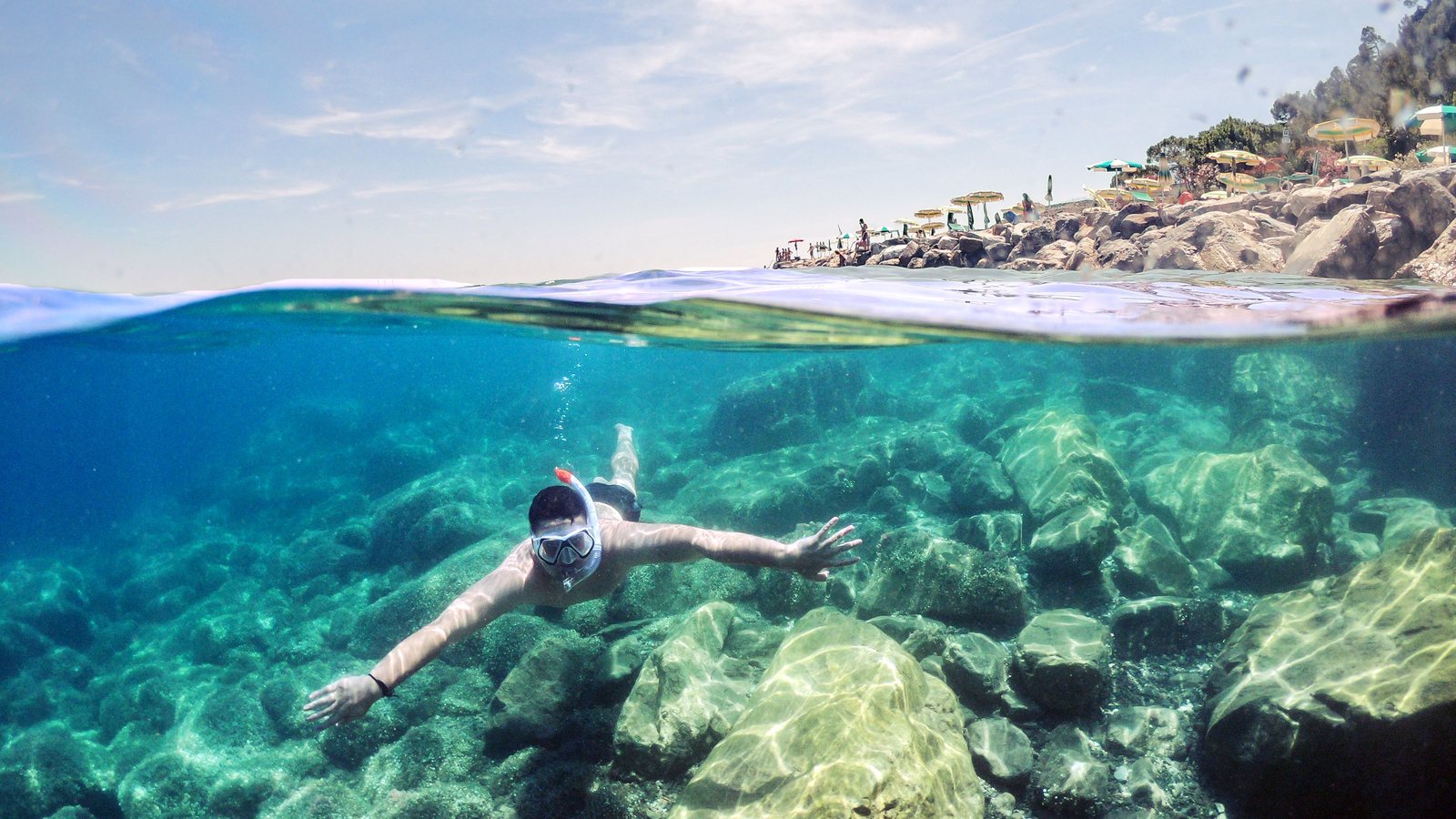 Schnorchler über Felsgrund in klarem Mittelmeer, halb über, halb unter Wasser fotografiert