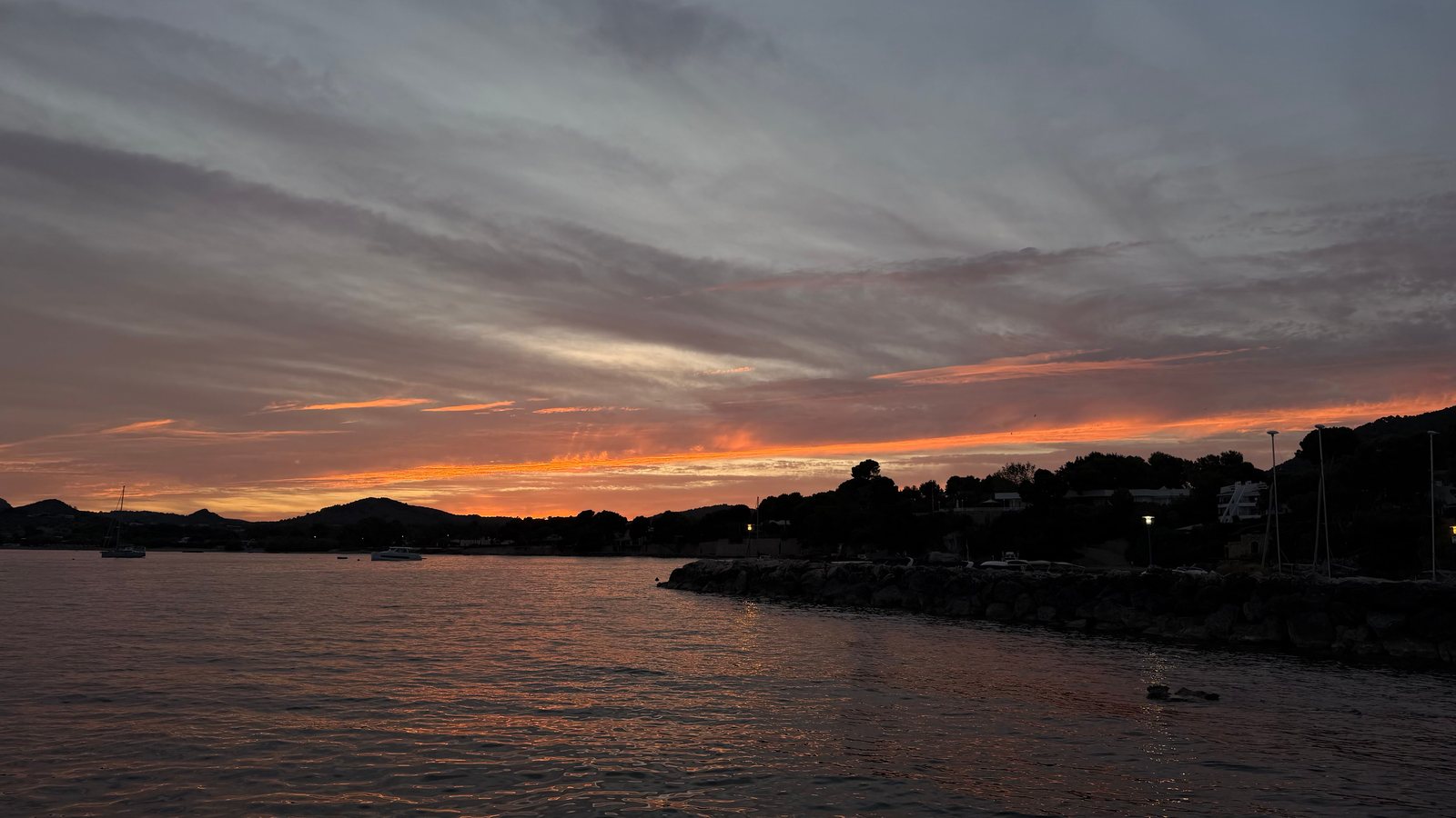 Sunset over a bay in Mallorca, boats and rocks on the shore silhouetted against the light