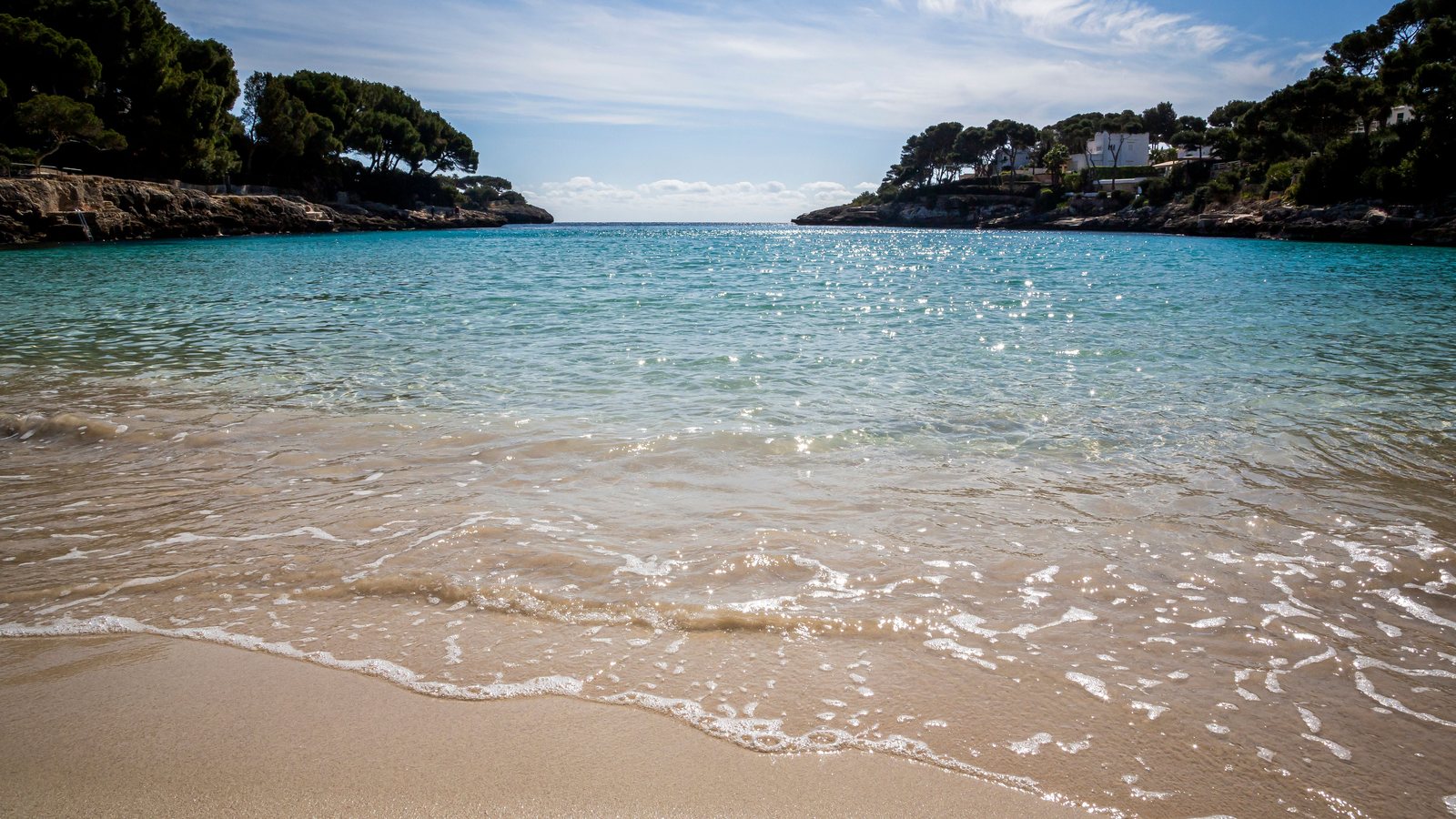 Kleine Bucht mit türkisfarbenem Wasser und hellem Sandstrand, an den Felsufern Pinien